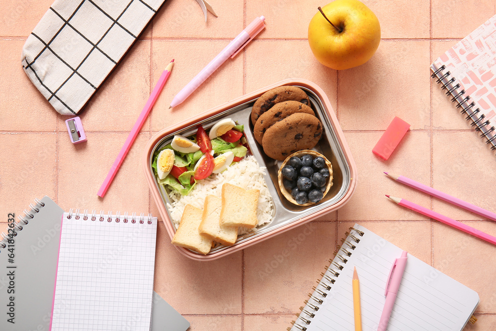 Lunchbox with delicious food and different stationery on orange tile background