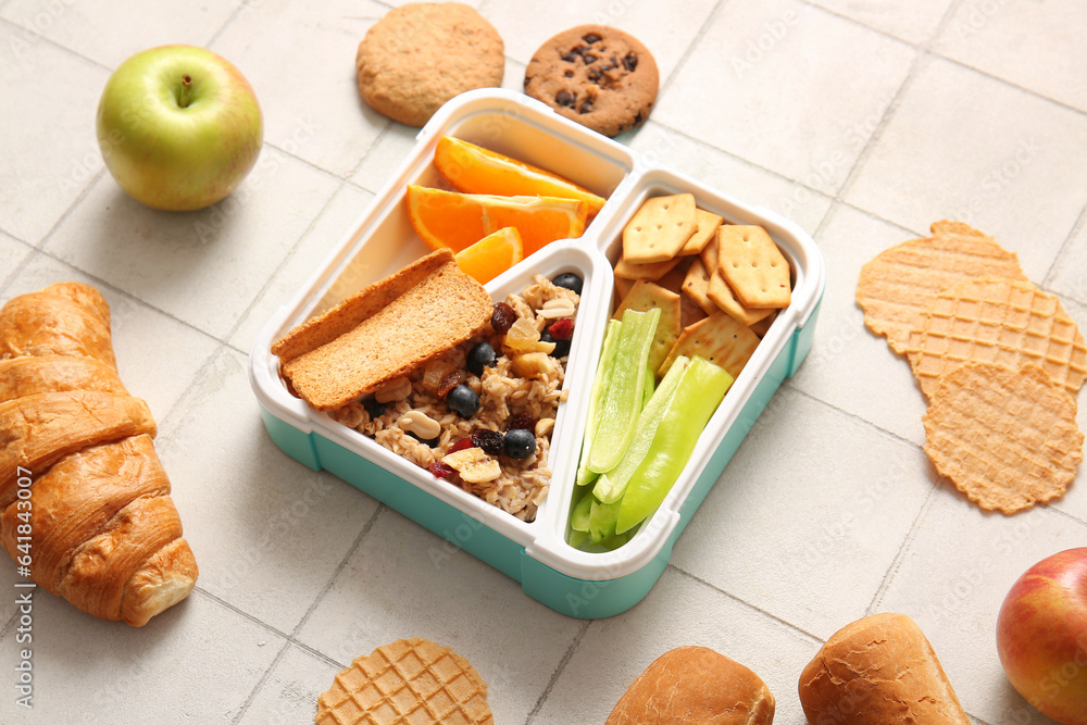 Lunchboxes with different delicious food on white tile background