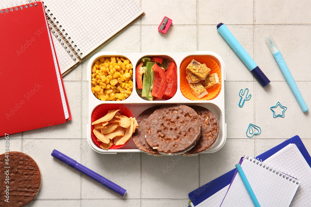 Lunchbox with delicious food and different stationery on white tile background