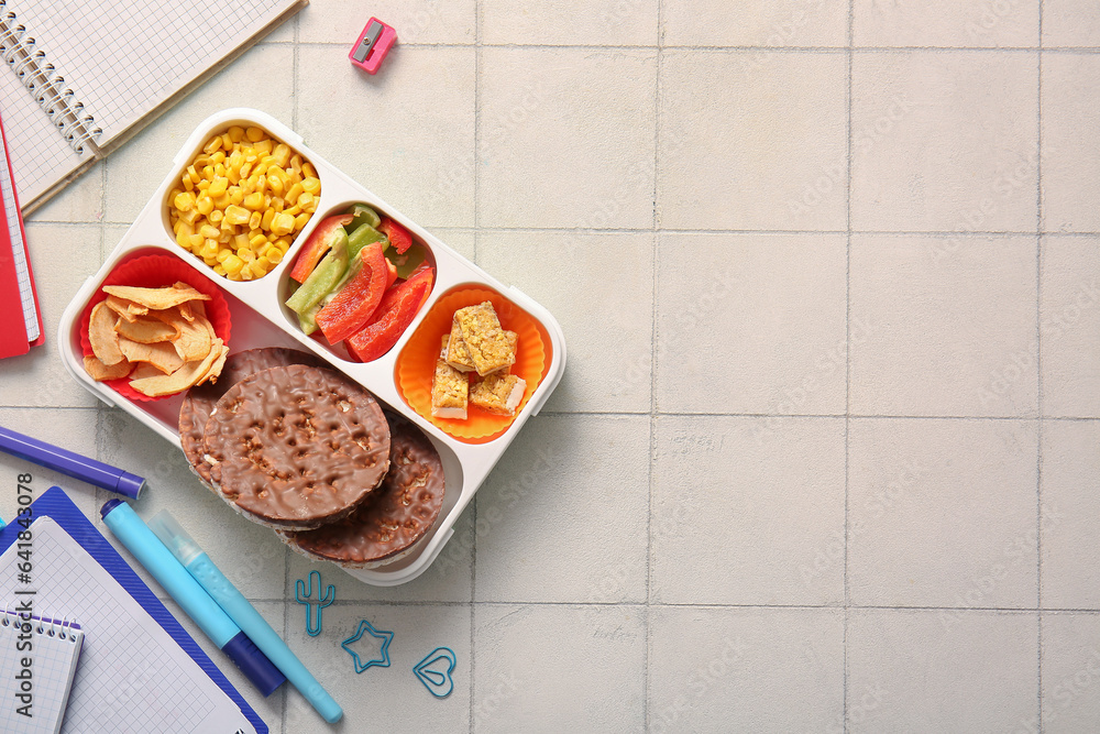 Lunchbox with delicious food and different stationery on white tile background