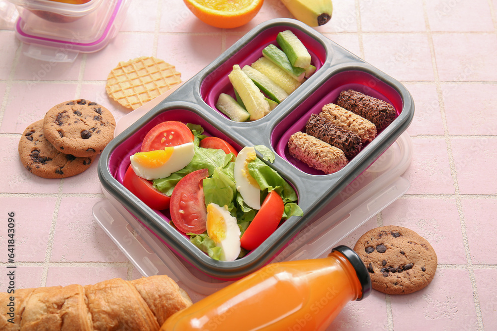 Lunchboxes with delicious food and bottle of juice on pink tile background