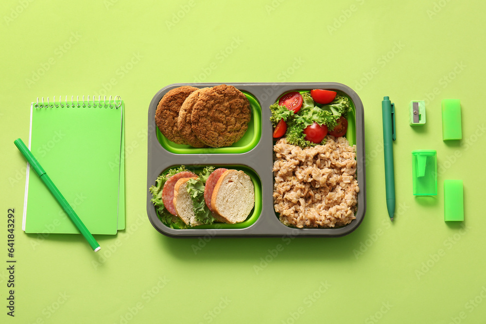 Lunchbox with delicious food and different stationery on green background