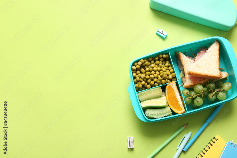 Lunchbox with delicious food and different stationery on green background