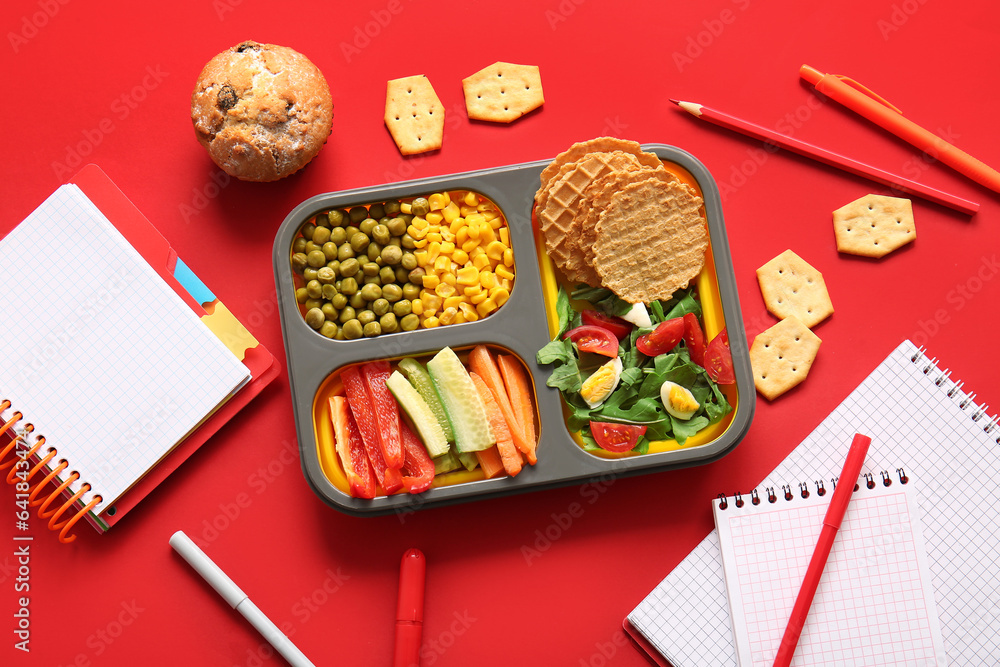 Lunchbox with delicious food and different stationery on red background