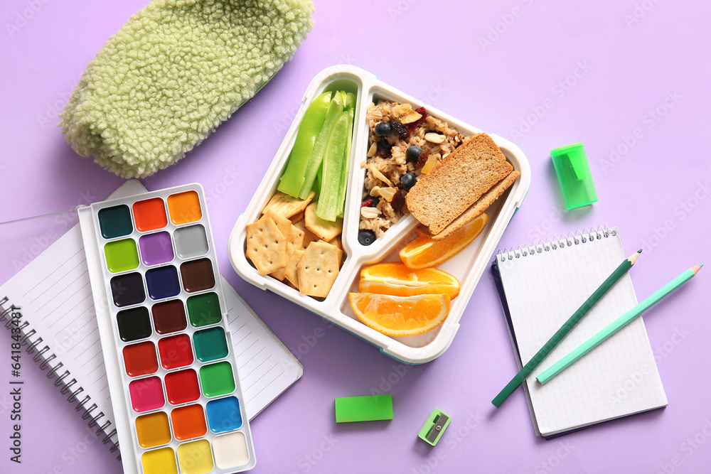 Lunchbox with delicious food and different stationery on lilac background