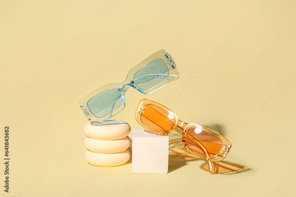 Decorative podiums with stylish sunglasses on yellow background