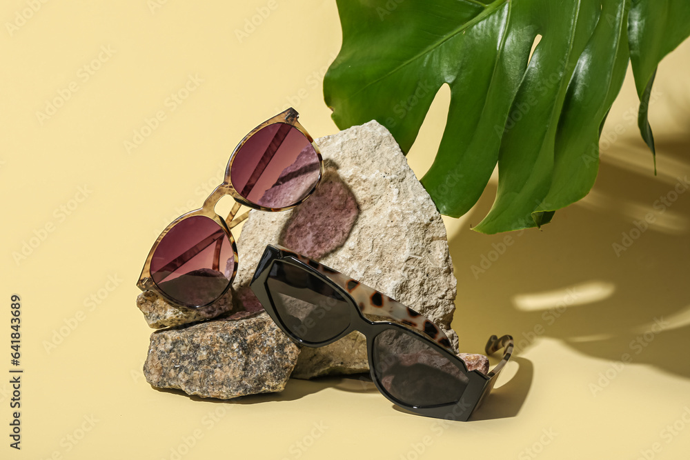 Stones with stylish sunglasses and monstera leaf on yellow background