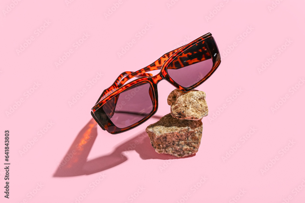 Stones with stylish sunglasses on pink background