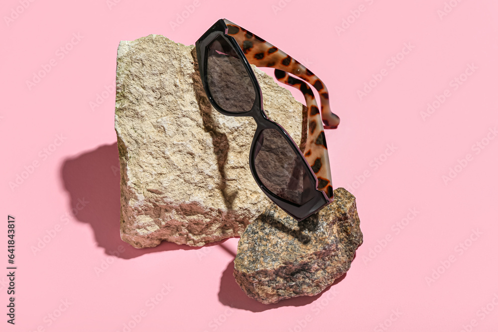 Stones with stylish sunglasses on pink background