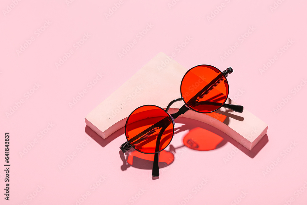 Decorative podium with stylish sunglasses on pink background