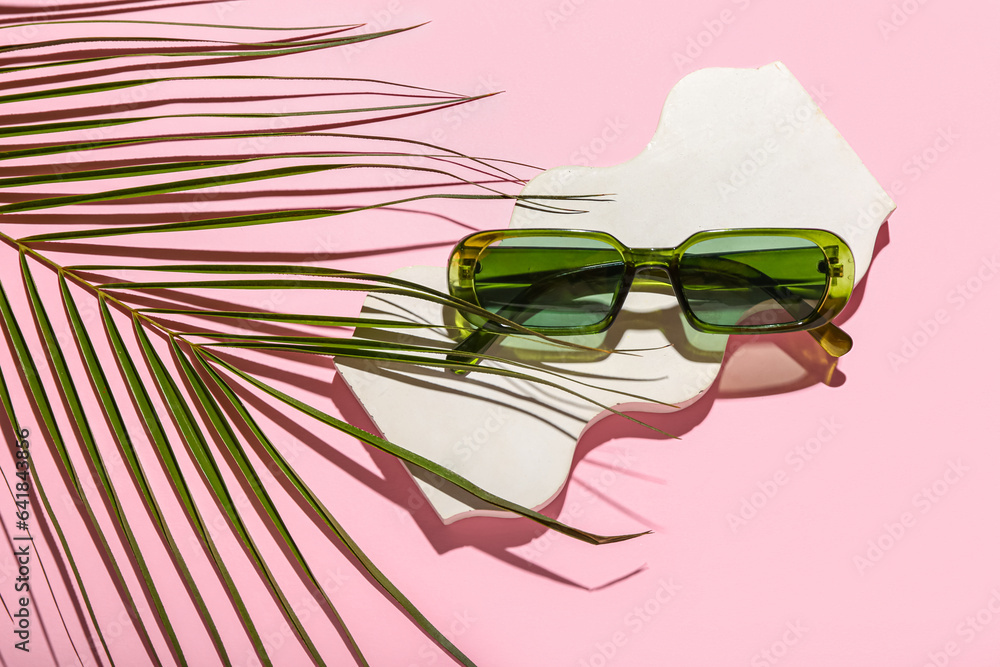 Decorative podium with stylish sunglasses and palm leaf on pink background