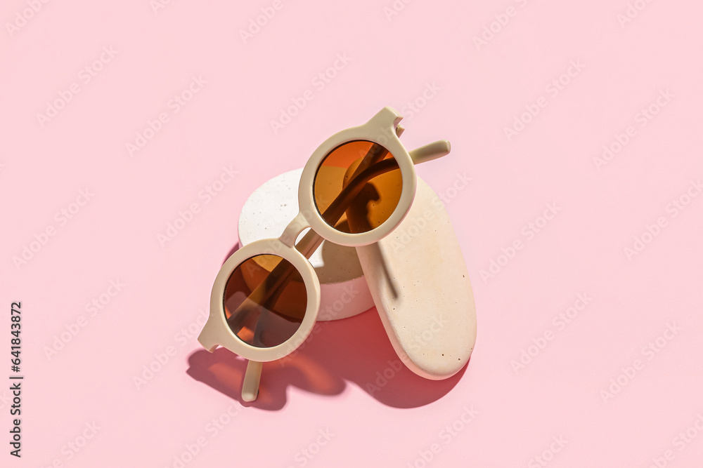 Decorative podium and stone with stylish sunglasses on pink background