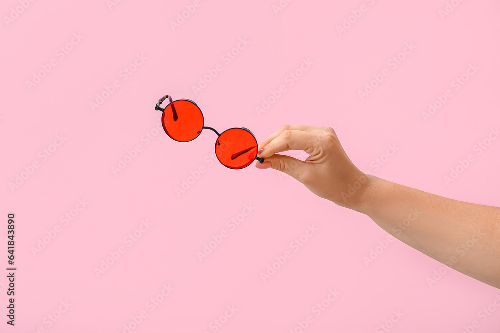 Woman holding stylish sunglasses on pink background