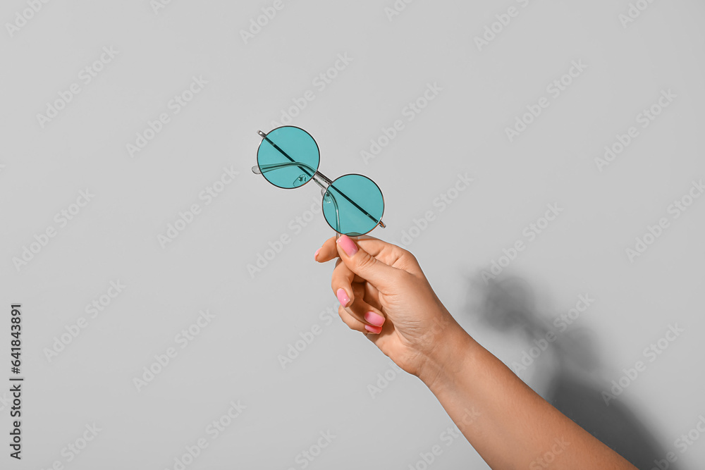 Woman holding stylish sunglasses on grey background