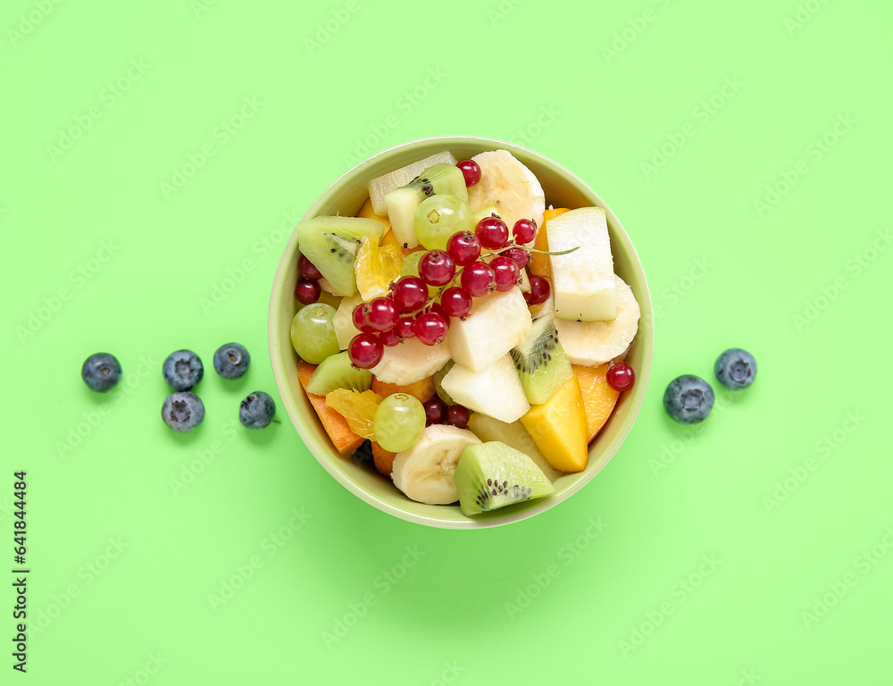 Bowl with fresh fruit salad on green background