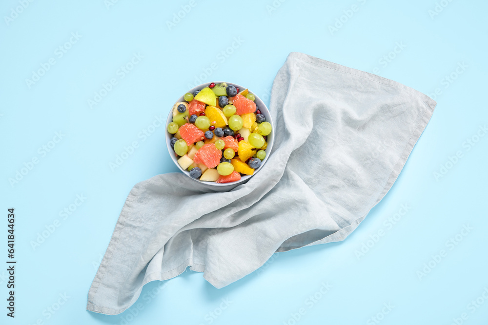 Bowl with fresh fruit salad on blue background