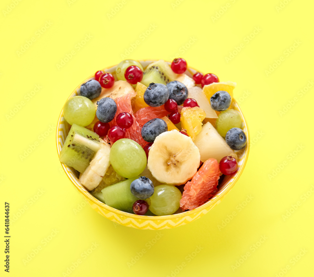 Bowl with fresh fruit salad on yellow background