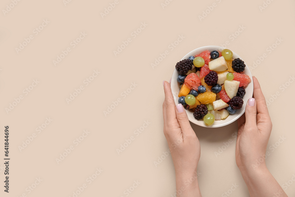 Woman with bowl of fresh fruit salad on beige background