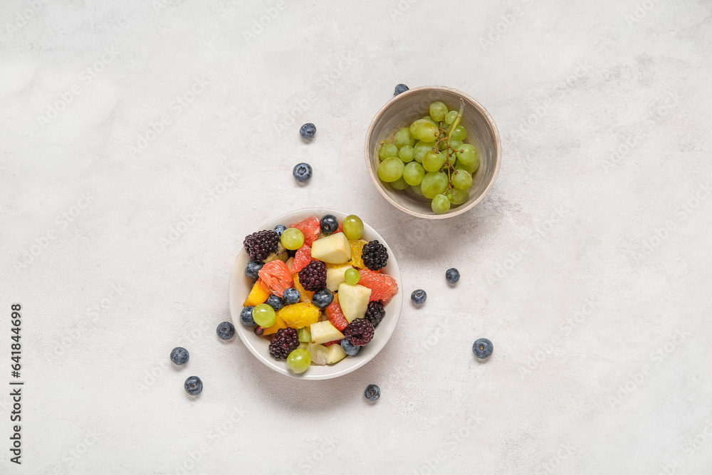 Bowl of fresh fruit salad and grapes on light background