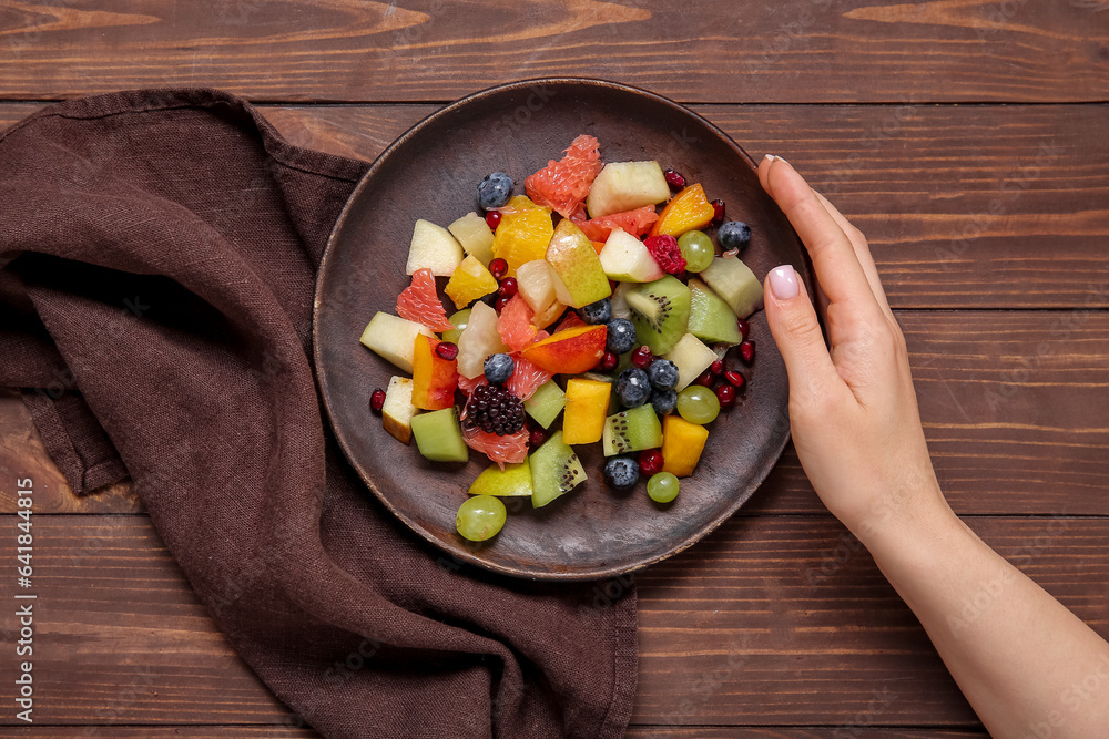 Woman with plate of fresh fruit salad on wooden background