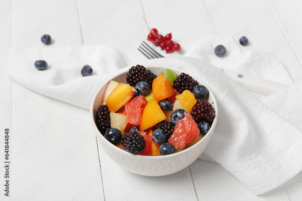 Bowl of fresh fruit salad on white wooden background