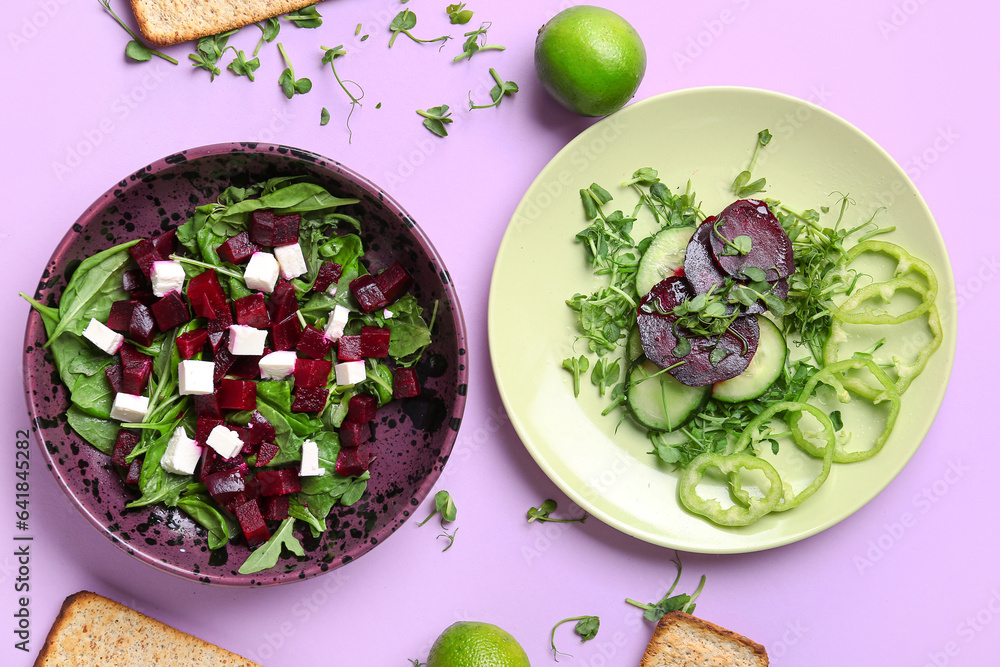 Bowl and plate of fresh vegetable salad with beet on lilac background