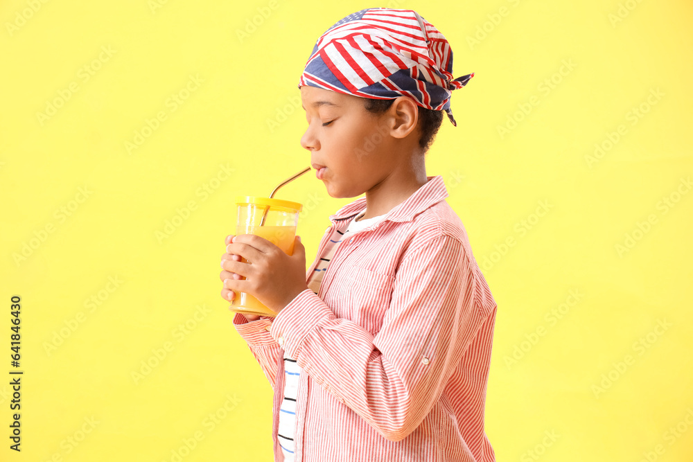 Little African-American boy with cup of fresh orange juice on yellow background