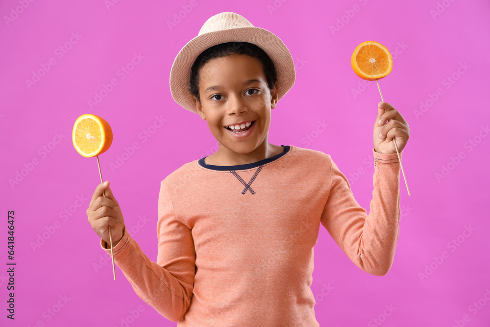 Little African-American boy with slices of orange on sticks against purple background