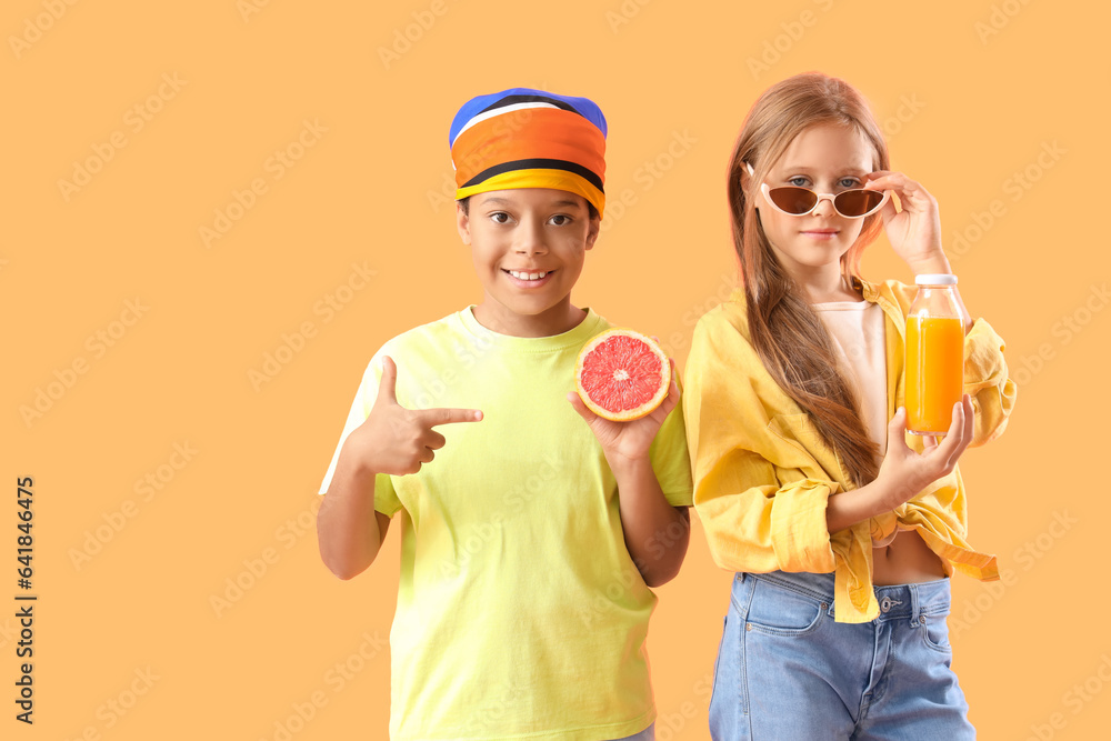 Little children with bottle of fresh citrus juice and grapefruit slice on orange background