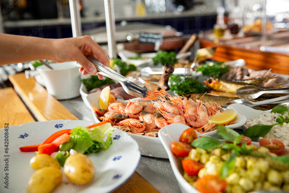 A restaurant customer puts delicious shrimp on a plate. Seafood buffet lunch in a cafe