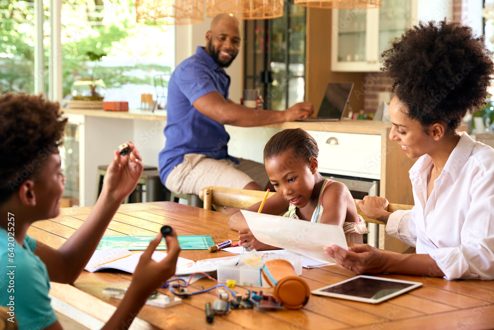 Family Around Table At Home Using Laptop With Parents Helping Children With Science Homework