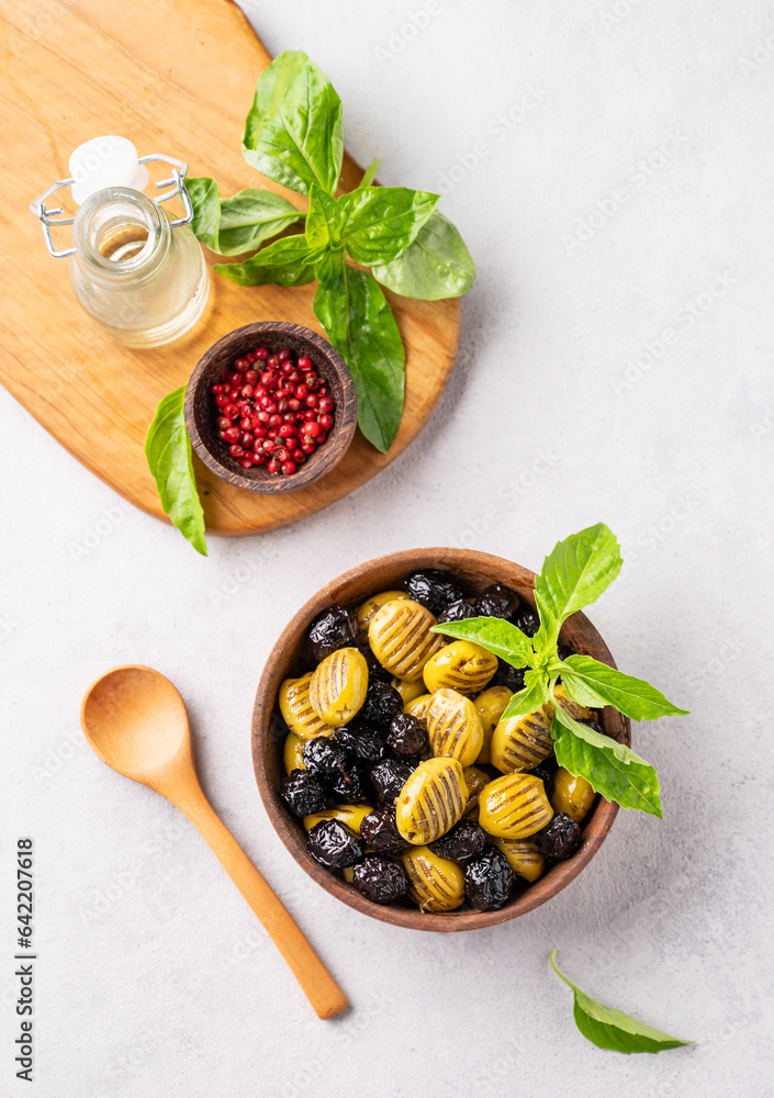 A set of green and black dried olives in wooden  bowl on a light background with olive oil and basil