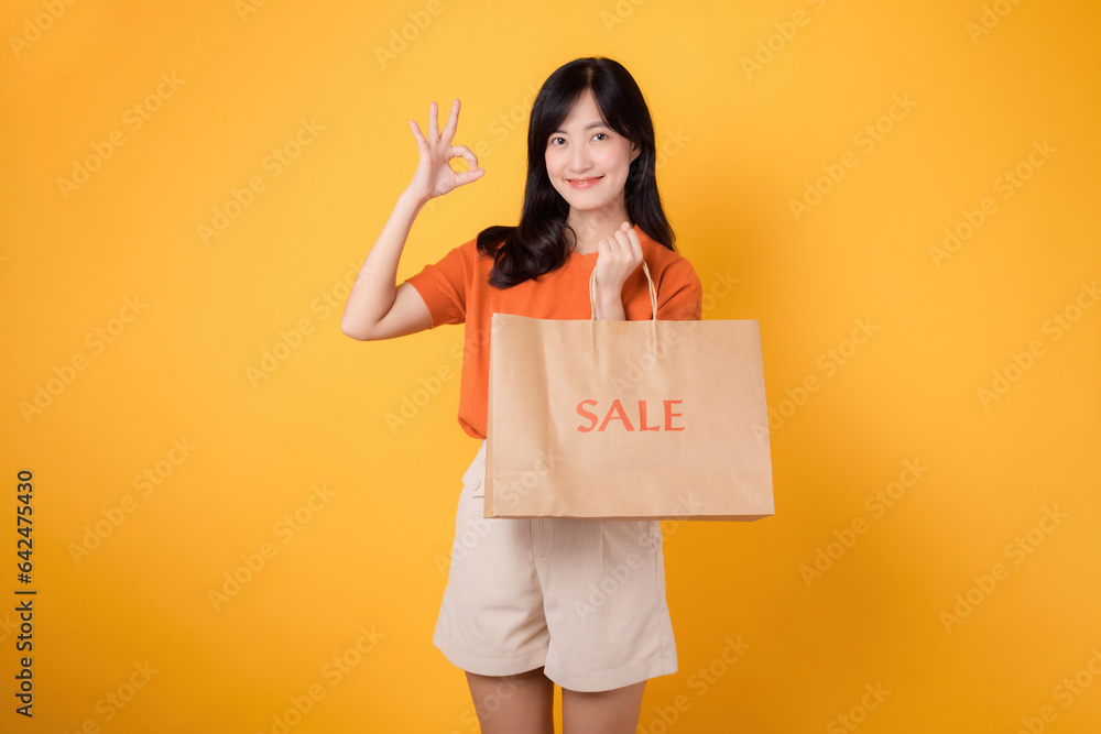 Celebrate savings and style in a shopping spree. Young woman holding a bag isolated on yellow backgr