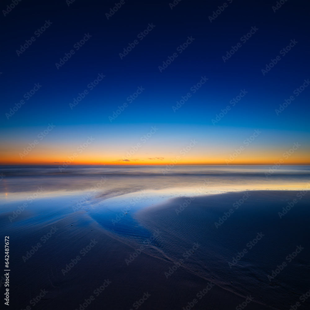 A seascape during sunset. Lines of sand on the seashore. Bright sky during sunset. A sandy beach at 