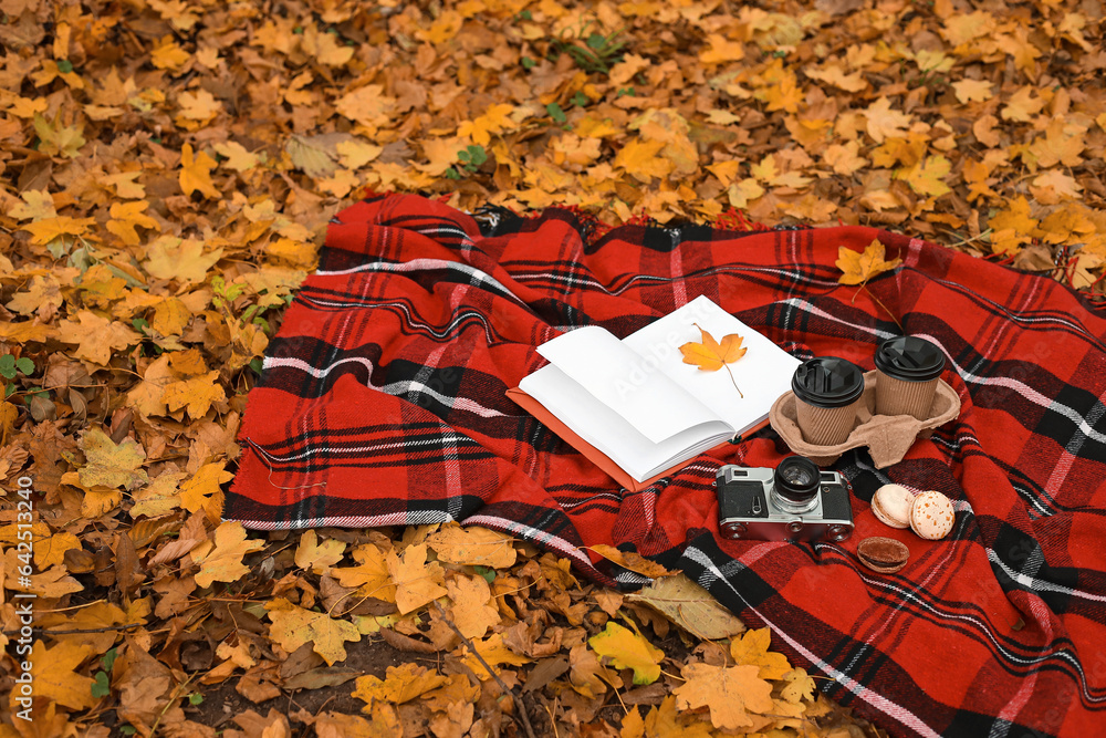 Book with autumn leaf, cups of coffee, macaroons and photo camera on plaid in park