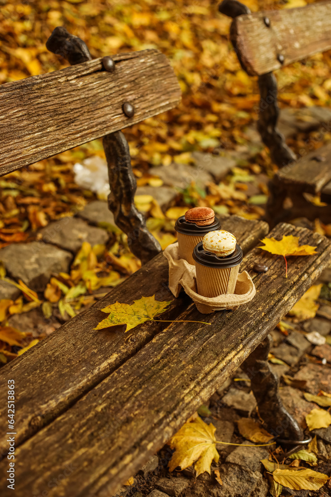 Cups of coffee with macaroons on bench in autumn park