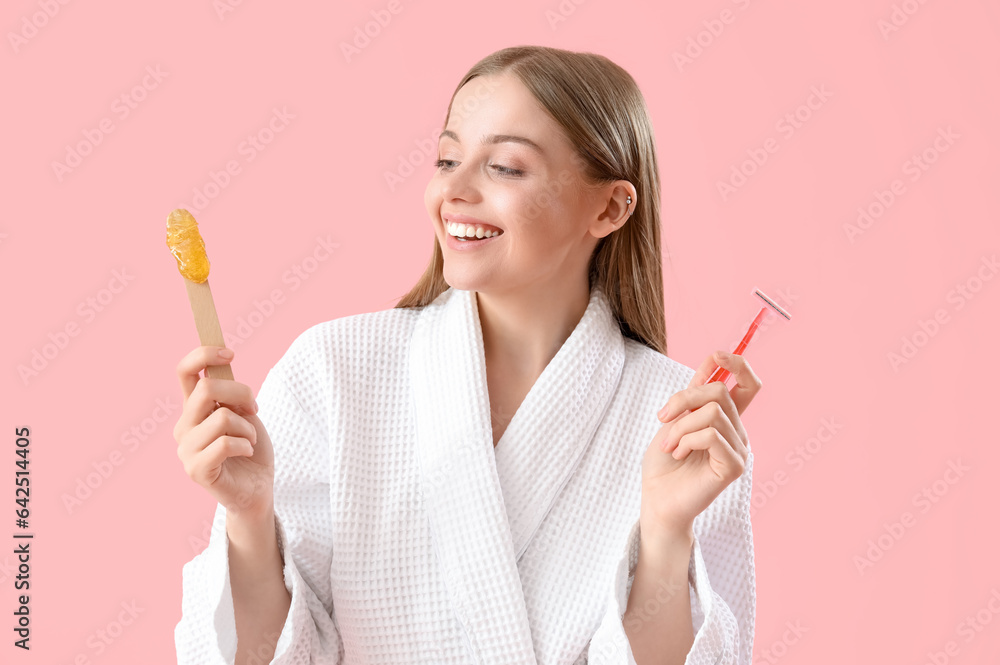 Young woman holding spatula with sugaring paste and razor on pink background