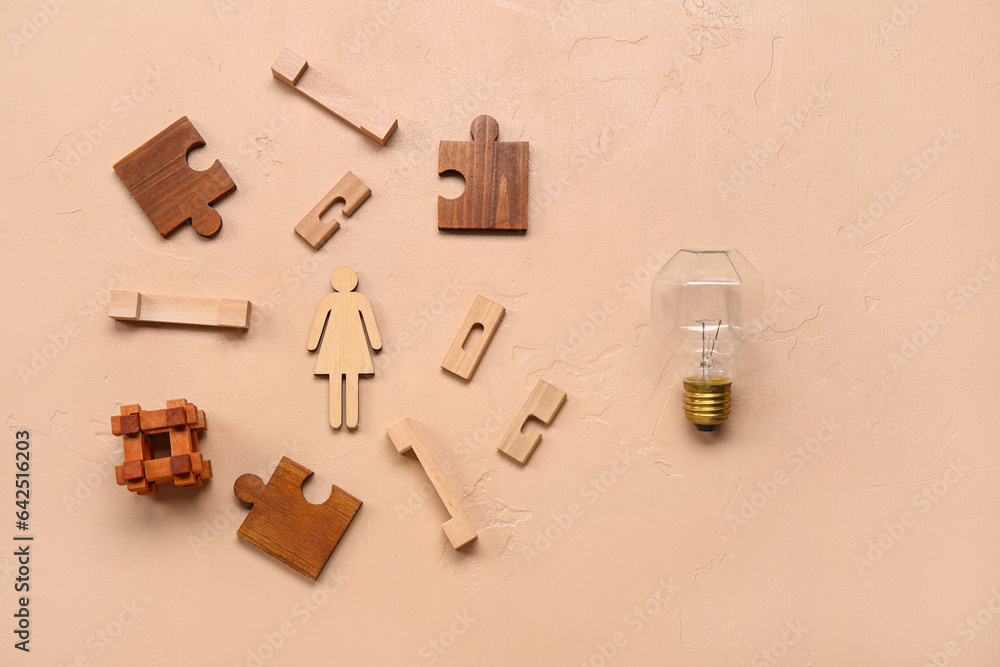 Wooden female figure with toys, puzzle pieces and light bulb on beige background. Logic concept