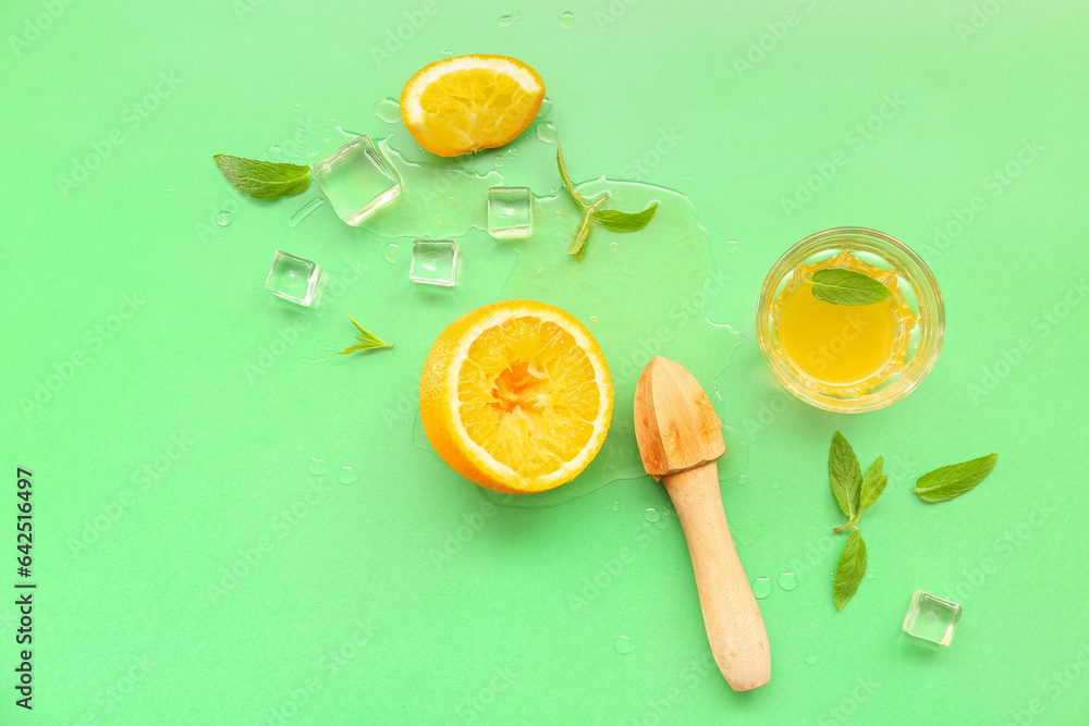 Orange with juicer, glass, ice cubes and mint on green background