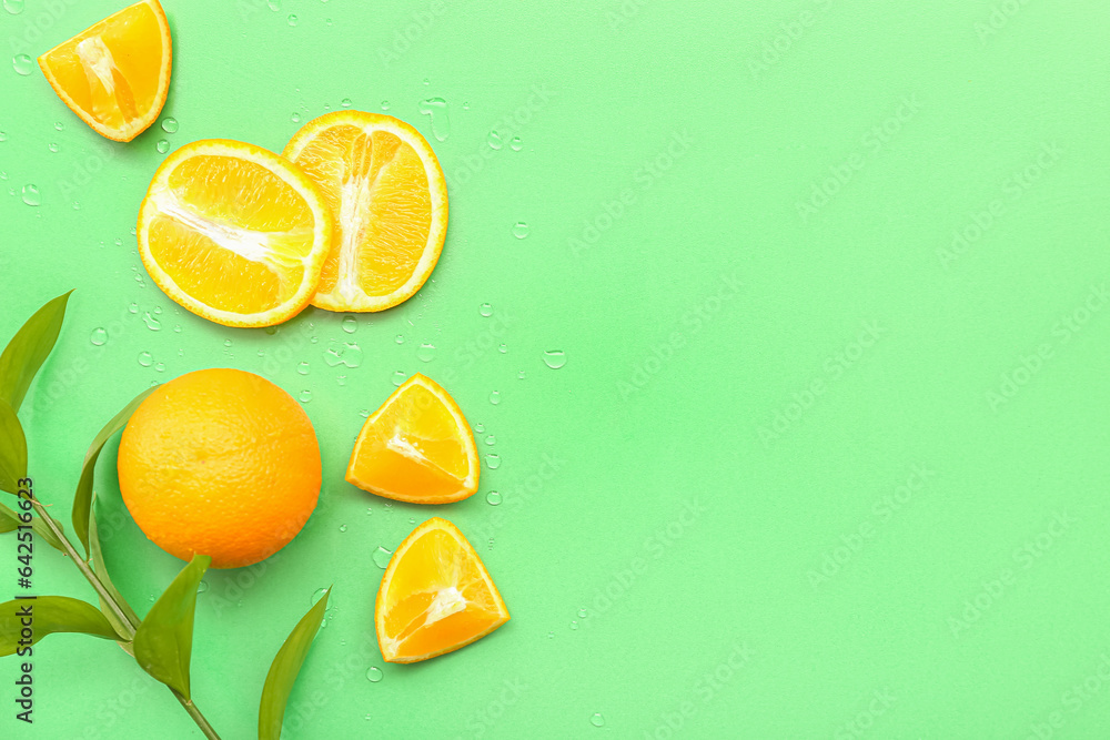 Cut orange with plant branch and water drops on green background