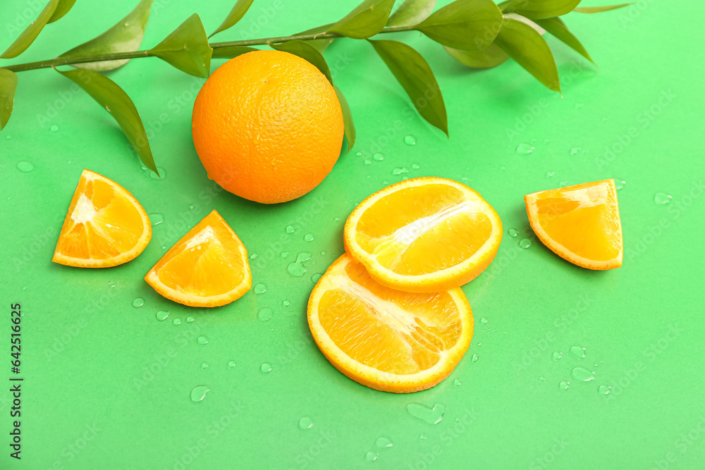 Cut orange with plant branch and water drops on green background