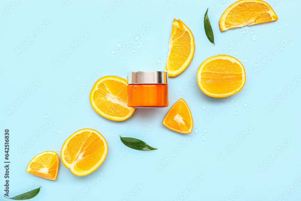 Jar of cream with cut orange and leaves on blue background