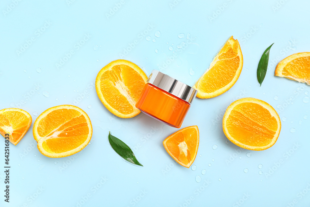 Jar of cream with cut orange and leaves on blue background