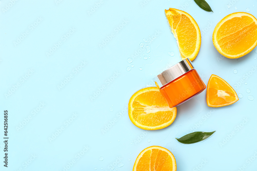 Jar of cream with cut orange and leaves on blue background