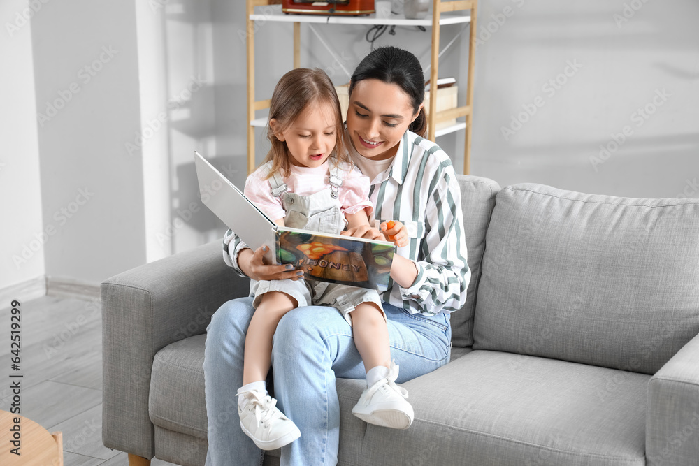 Young woman reading story to her little daughter at home