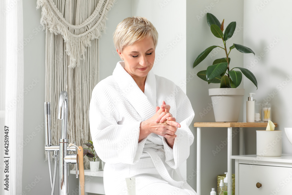 Mature woman applying hand cream in bathroom