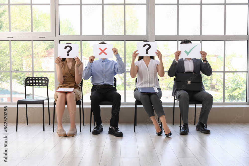 Young people holding paper sheets with different marks while waiting for job interview in office