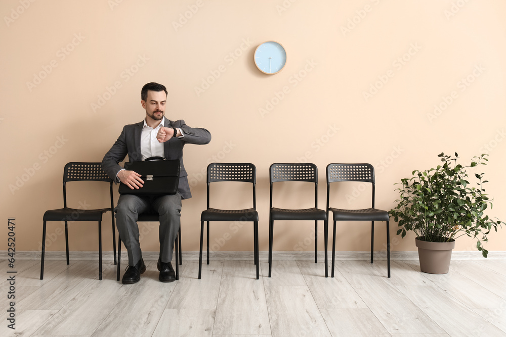 Young man looking at wristwatch while waiting for job interview in office