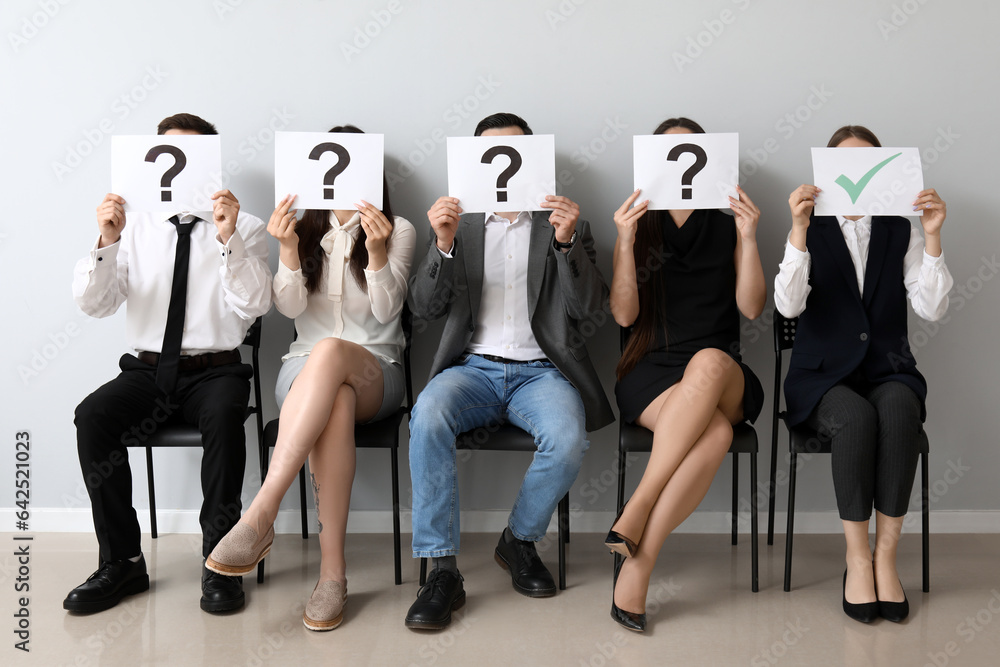 Young applicants holding paper sheets with check and question marks in room