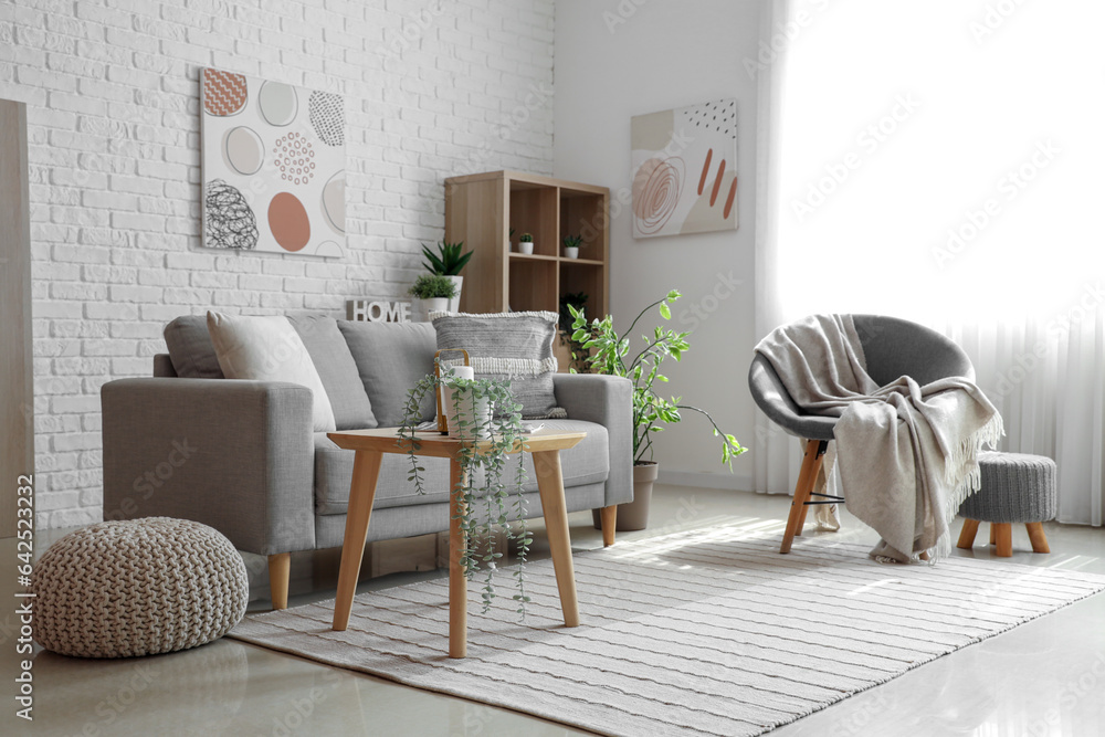 Interior of light living room with cozy grey sofa, armchair and coffee table